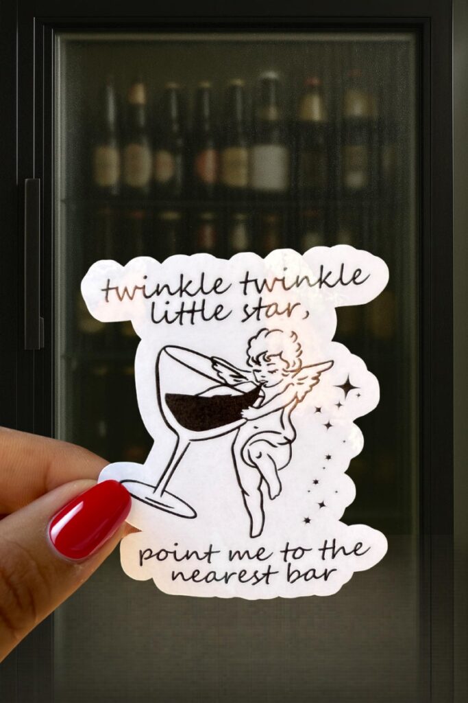 Sticker of a cherub dipping its foot into a wine glass, surrounded by stars, with the phrase “twinkle twinkle little star, point me to the nearest bar.”